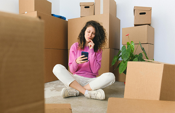Woman browsing on her mobile sitting around boxes